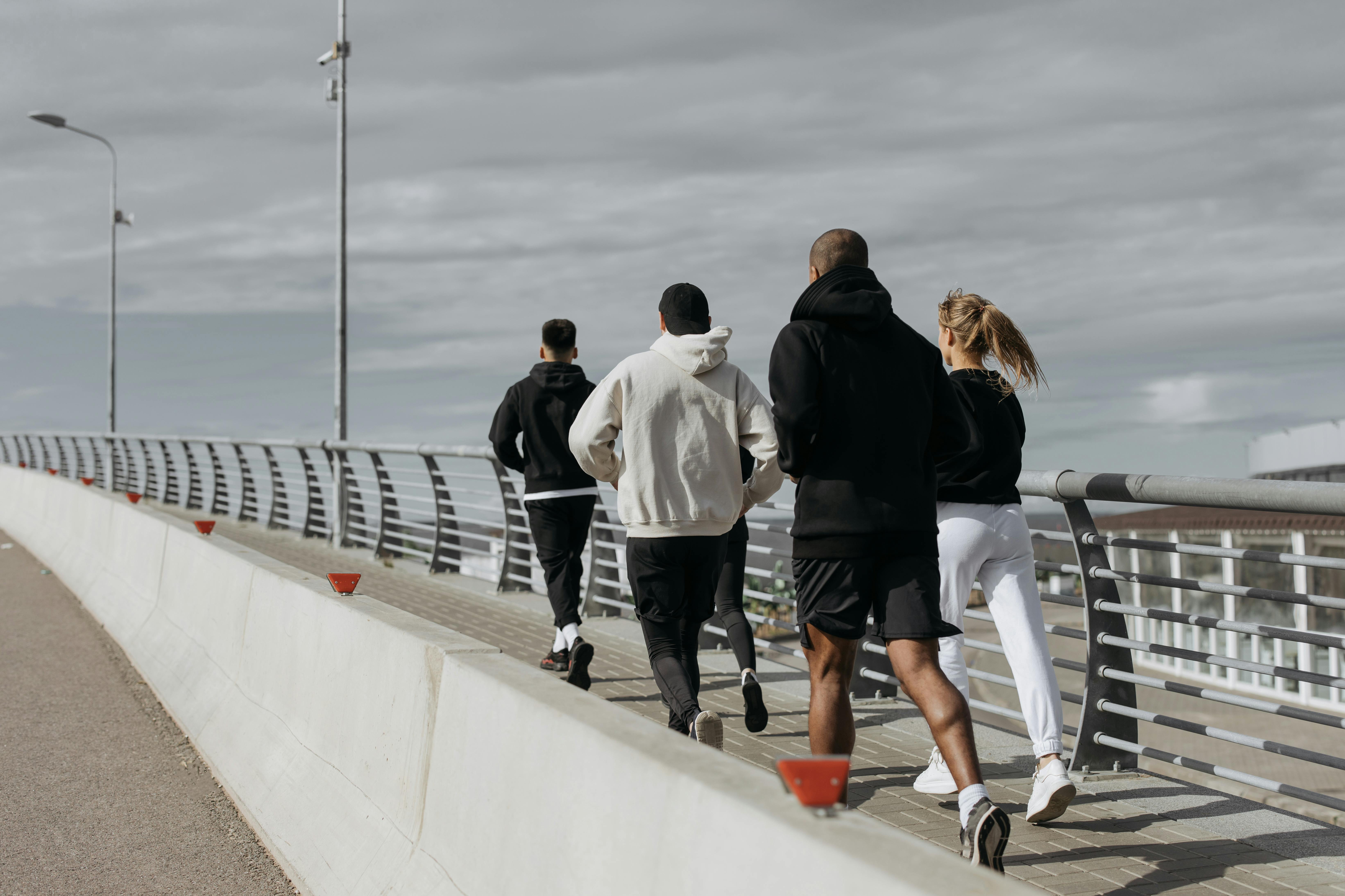 Group of runners in athletic wear jogging together on a walkway with a railing under a cloudy sky.