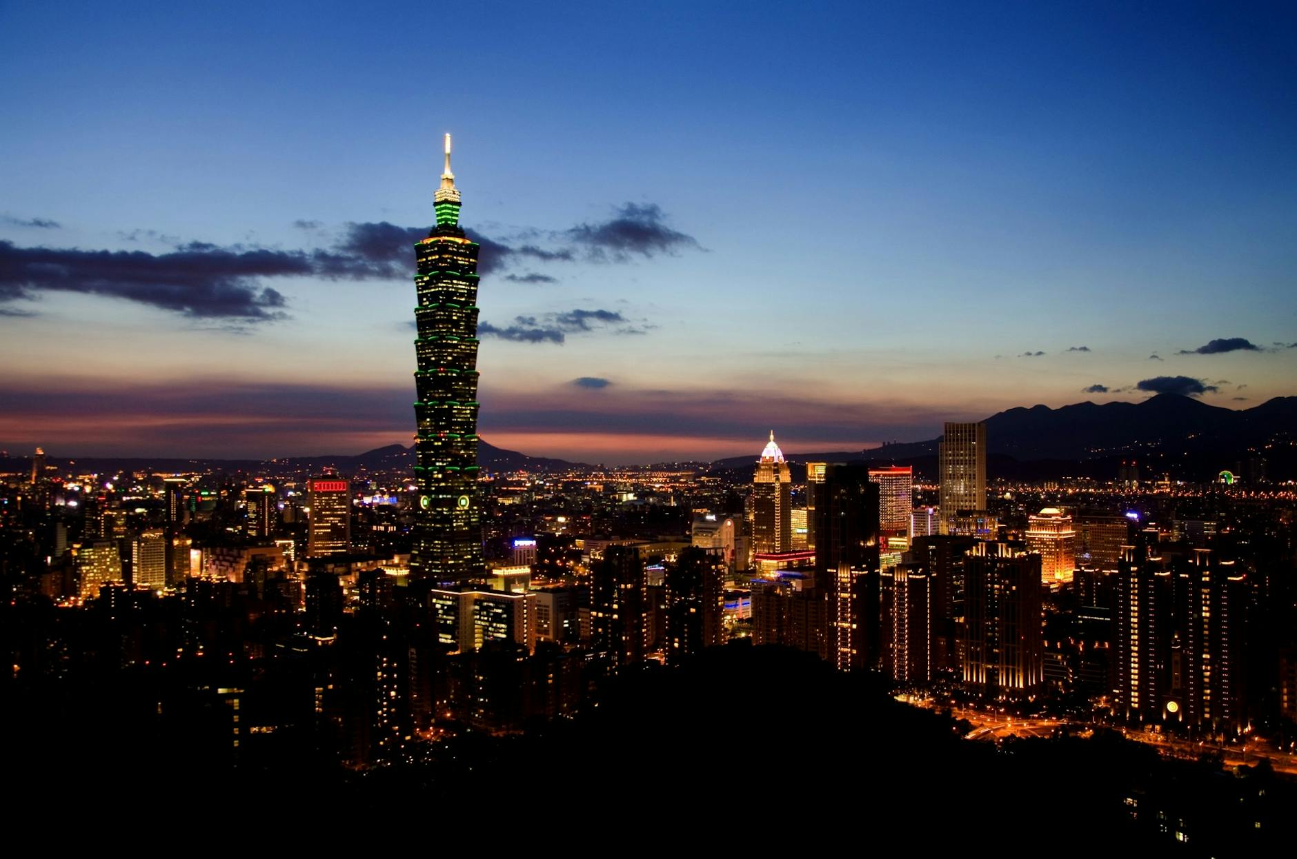 A panoramic view of Taipei, Taiwan at dusk, showcasing the iconic Taipei 101 skyscraper illuminated against a colorful sky.
