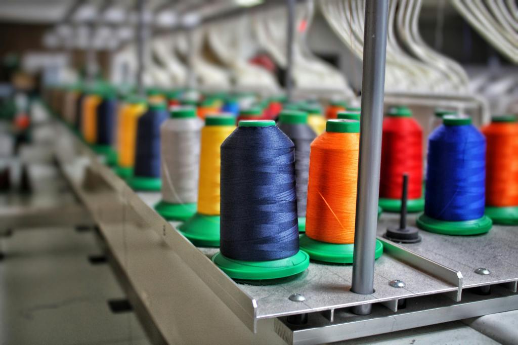 Colorful spools of thread arranged in a sewing workshop, showcasing various thread colors on green spools.